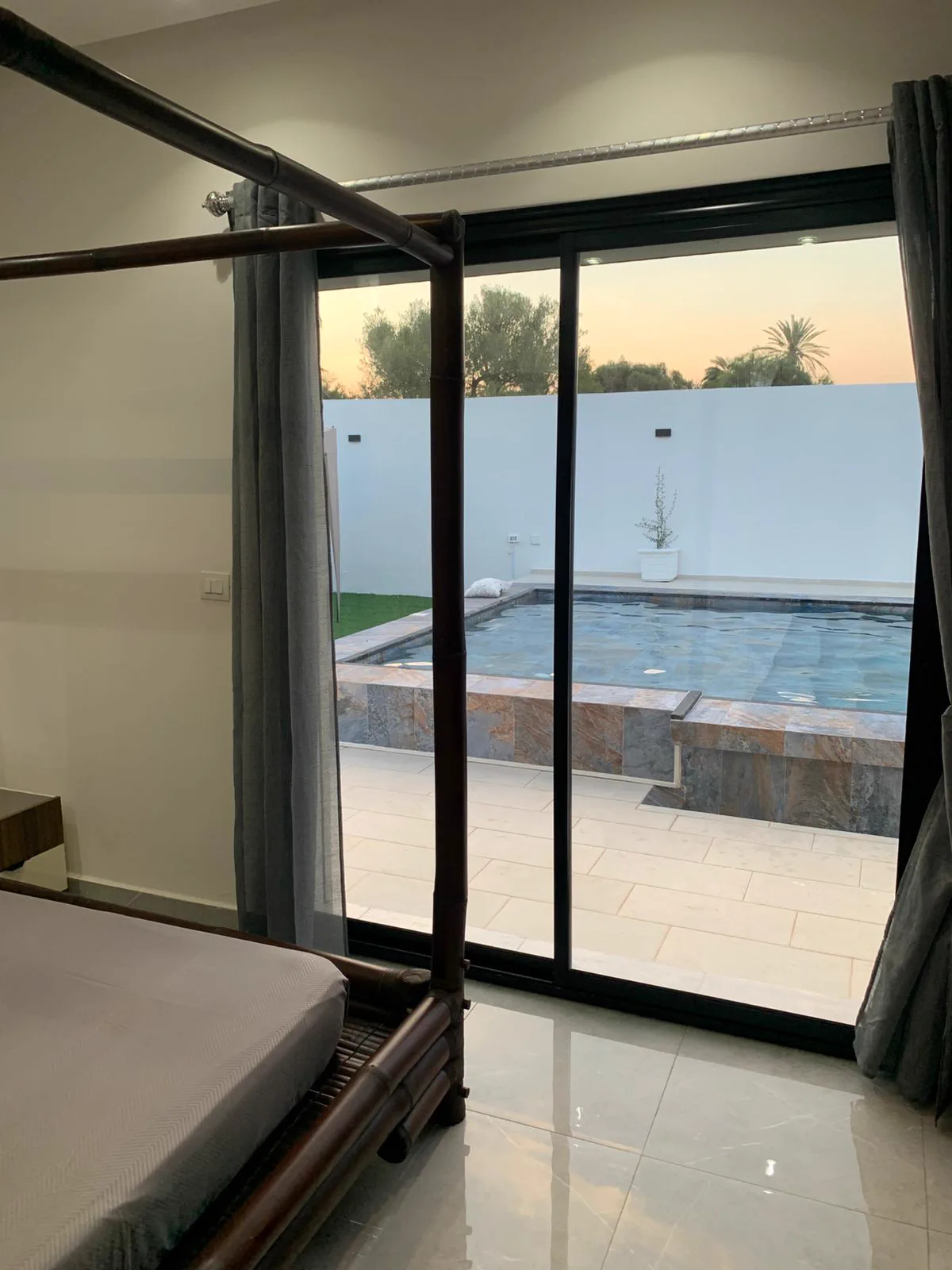 Suite parentale avec lit baldaquin en bambou et vue sur la piscine au coucher du soleil